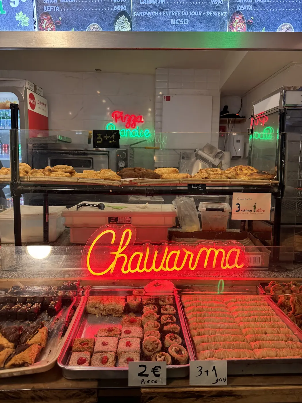 Le comptoir sous le néon rouge Chawarma, avec les pâtisseries orientales en vitrine